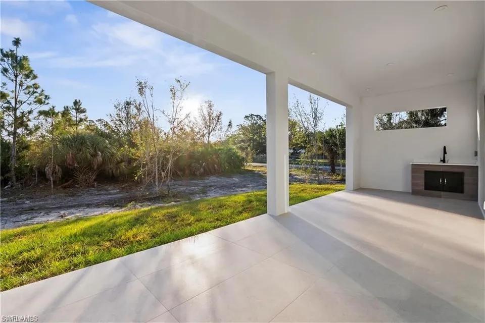 Expansive covered patio featuring light-toned tile flooring, recessed lighting, and an outdoor kitchen with wood-finish cabinetry, a stone-look countertop, and a built-in sink with a matte black faucet