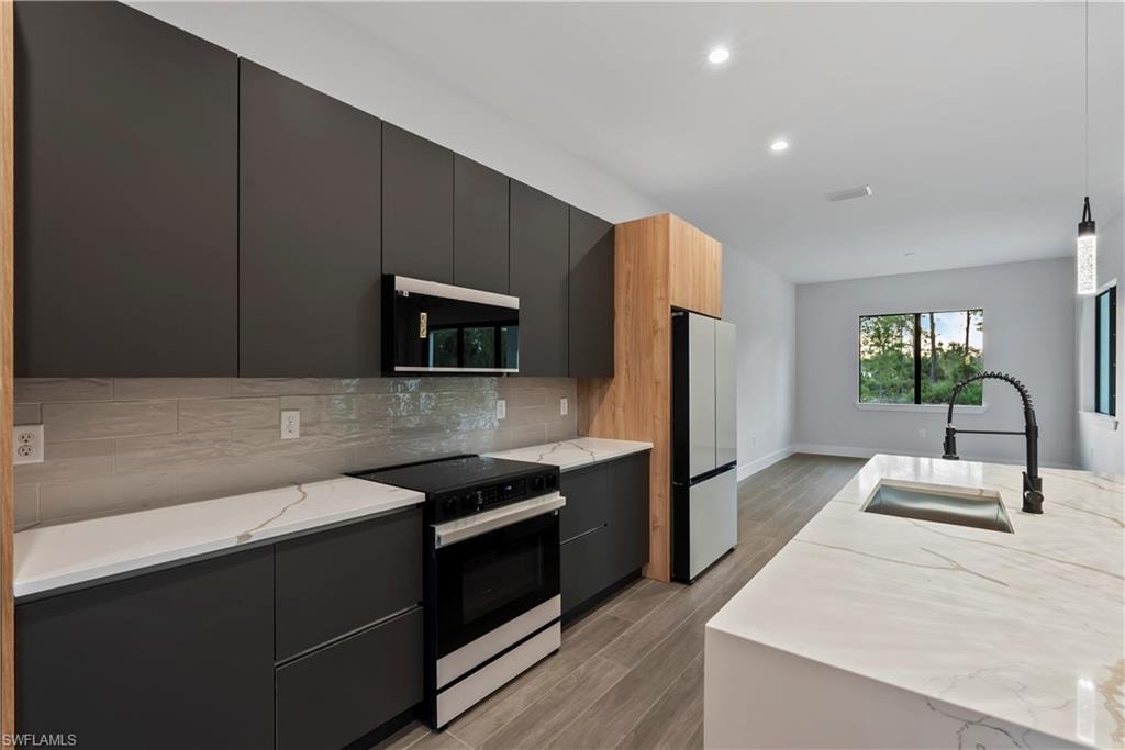 Modern kitchen with dark flat-panel cabinetry, white stone countertops, stainless steel appliances, and a large center island featuring an undermount sink and gooseneck faucet