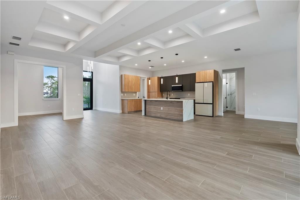 Open-concept living space featuring wood-look tile flooring, coffered ceilings with recessed lighting, and a kitchen island with a waterfall countertop