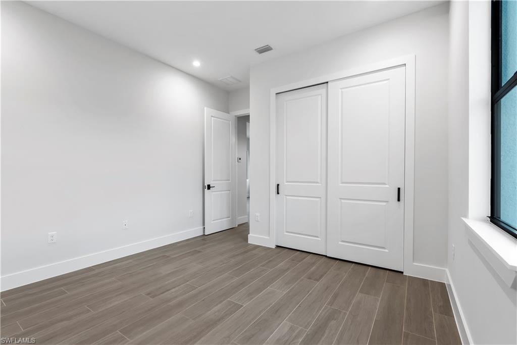 Wood-look plank flooring, white walls, recessed ceiling lighting, a white panel door, and sliding panel closet doors with matte black hardware