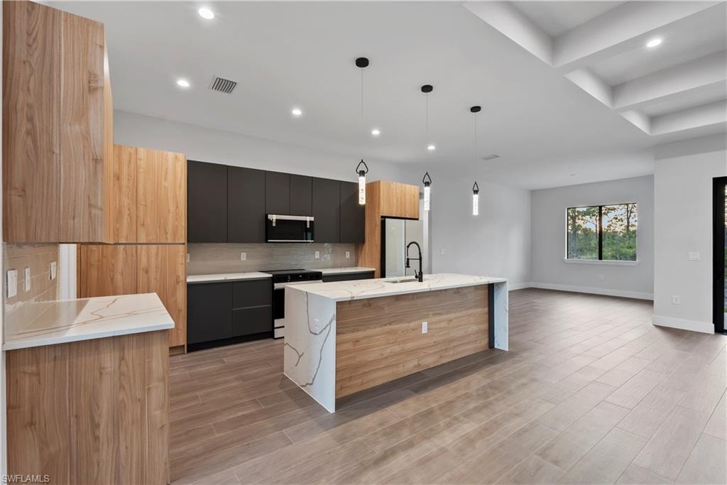 Kitchen featuring a waterfall island with stone countertop, wood-finish cabinetry, built-in stainless steel appliances, and recessed lighting