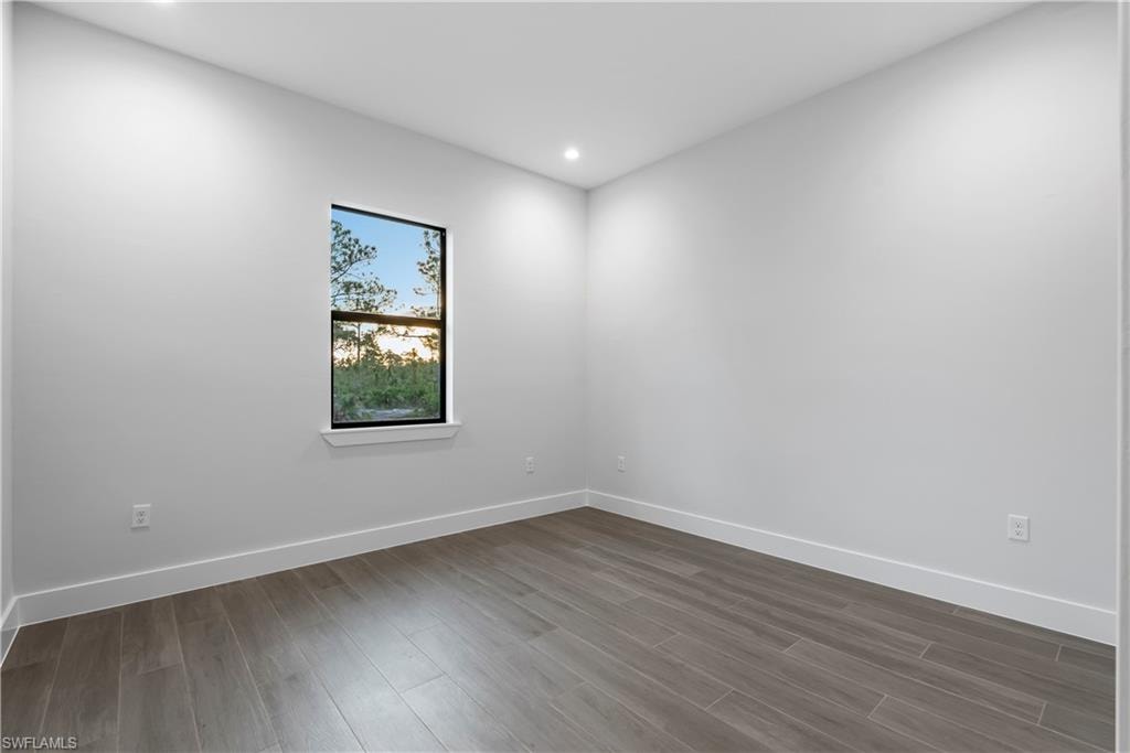 Recessed lighting, wood-finish flooring, white walls, and a single window with black trim