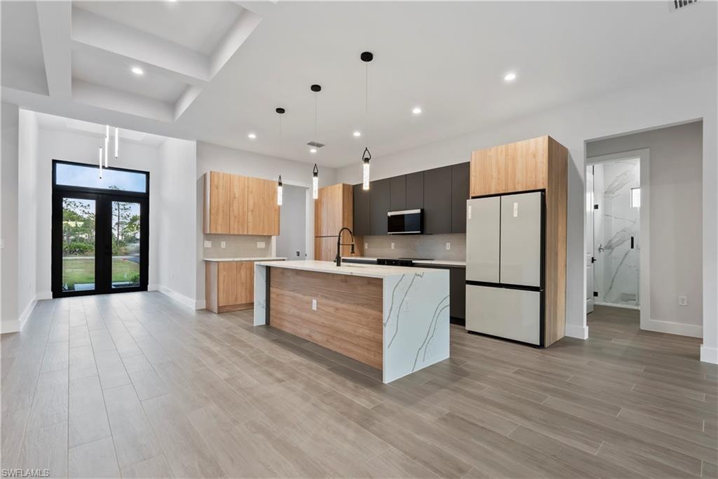 Open concept kitchen and living area featuring a waterfall island with stone countertop, integrated stainless steel appliances, wood-finish flooring, and a tray ceiling with recessed lighting