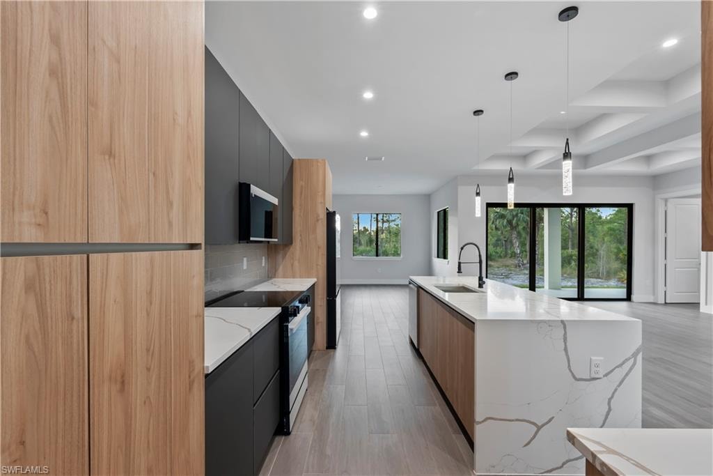 Kitchen featuring wood-finish paneling, matte black cabinetry, light stone countertops, and an integrated kitchen island with a sink