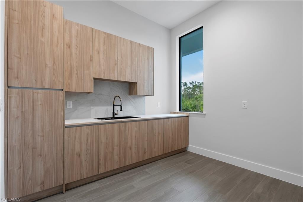 Wood-finish cabinetry, integrated refrigerator, white countertop, black sink, and a modern window