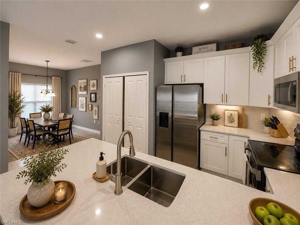 Kitchen featuring light-toned countertops, white cabinetry with gold-toned hardware, stainless steel appliances, and tile backsplash