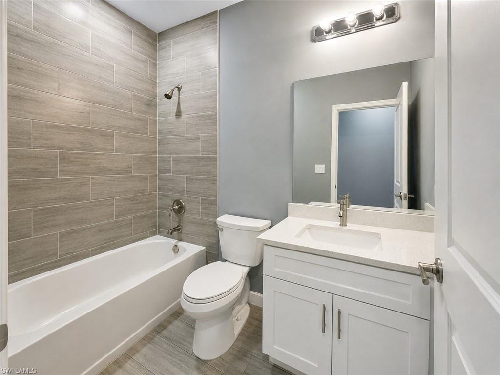 Bathroom featuring a white vanity with a light-colored countertop, an undermount sink, a large wall-mounted mirror, and a white bathtub with tile surround