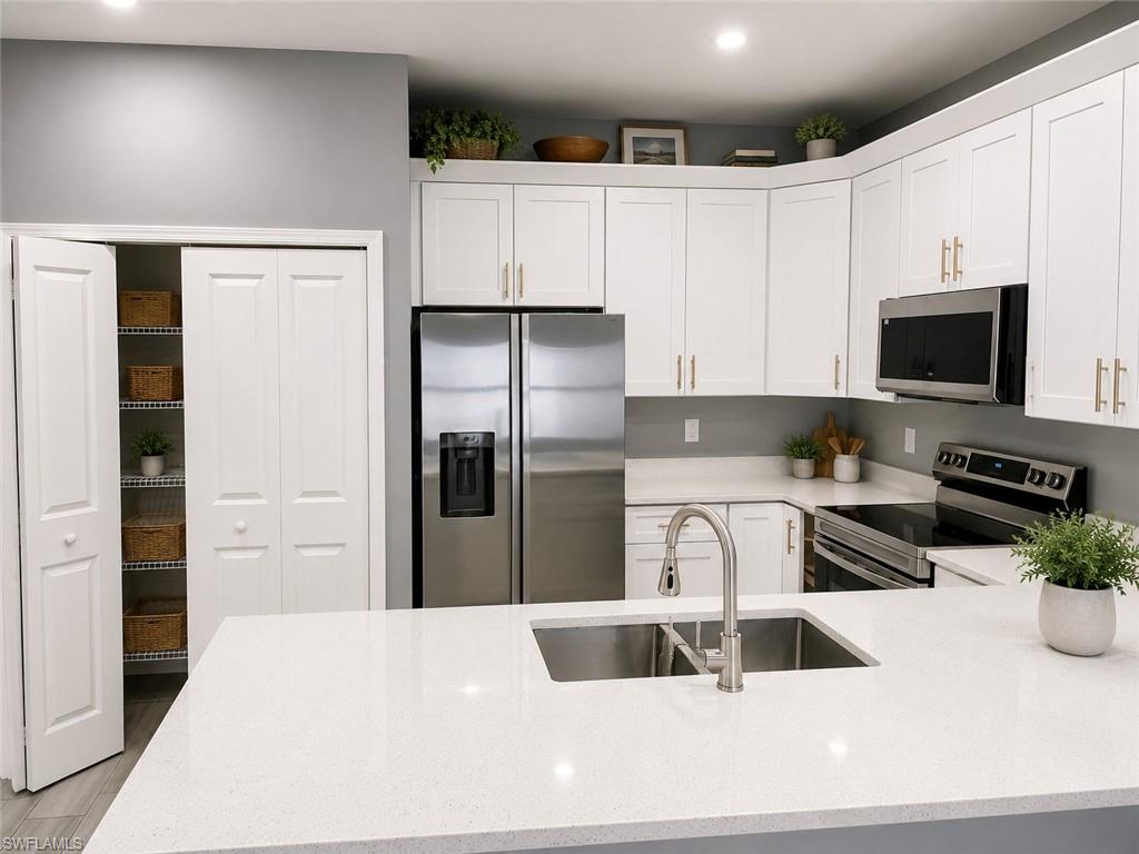 Modern kitchen featuring white shaker cabinetry, stainless steel appliances, a large center island with an undermount sink, and a pantry with bi-fold doors