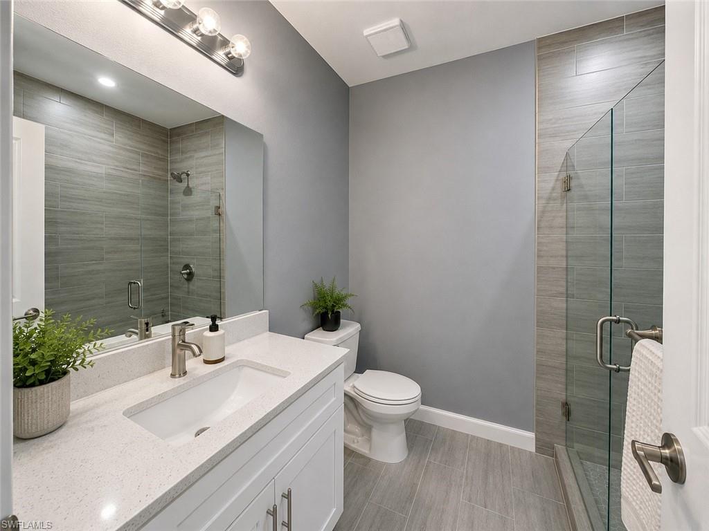 Modern bathroom featuring a quartz vanity countertop, white cabinetry, undermount sink, and a glass-enclosed shower with tiled walls and flooring