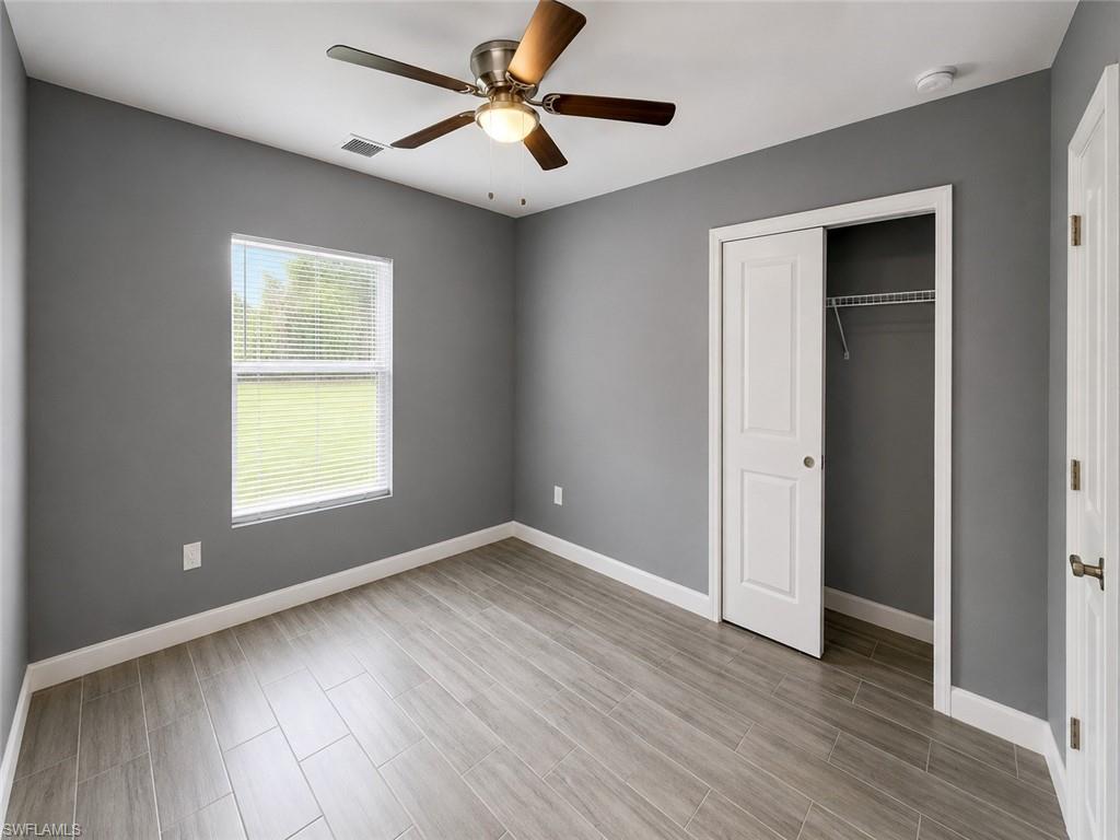 Wood-finish flooring, ceiling fan with integrated lighting, window with blinds, and sliding closet doors