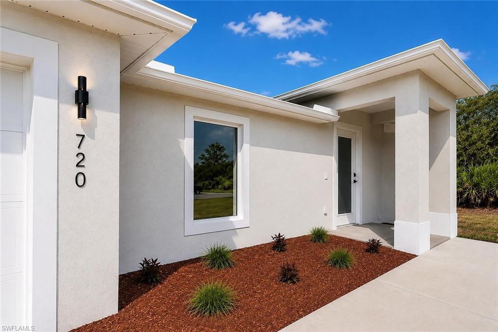 Smooth stucco exterior with a covered entry, modern exterior lighting, and a white framed window