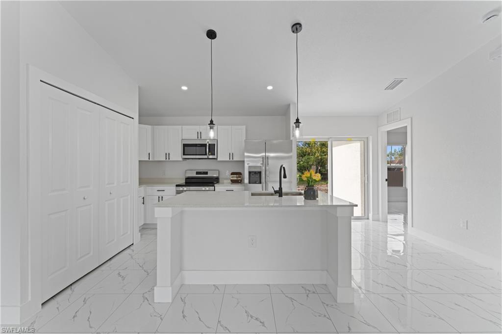 Contemporary kitchen featuring white cabinetry, stainless steel appliances, a center island with sink, and pendant lighting