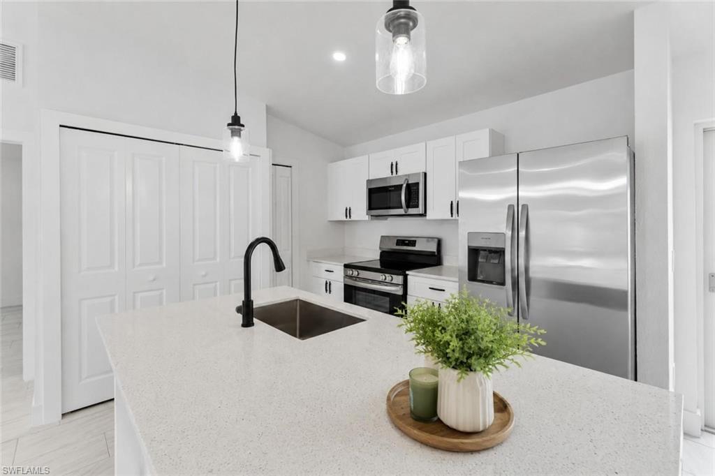 Kitchen featuring a large island with an undermount sink, white cabinetry with dark hardware, stainless steel appliances, and pendant lighting