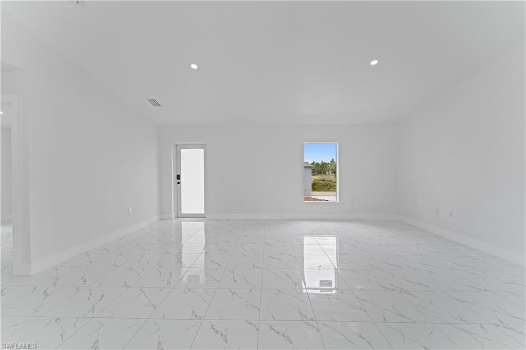 Spacious room featuring white walls, large format tile flooring, recessed lighting, and a glass-paneled door
