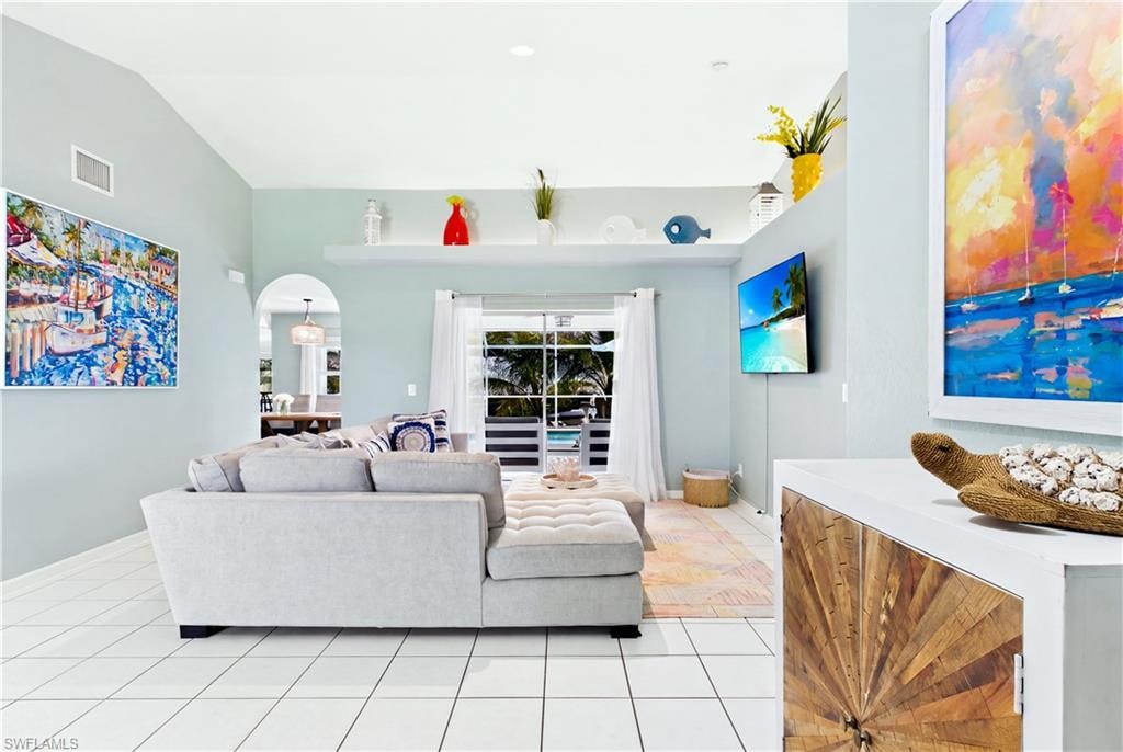 Vaulted ceiling, white tile flooring, arched doorway, sliding glass doors, built-in shelving.