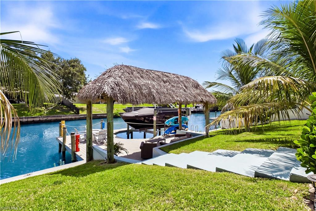 Expansive waterfront with a private dock featuring a boat lift, covered tiki hut, and concrete steps leading to the water. THIS IS WHAT FL LIVING IS ALL ABOUT!