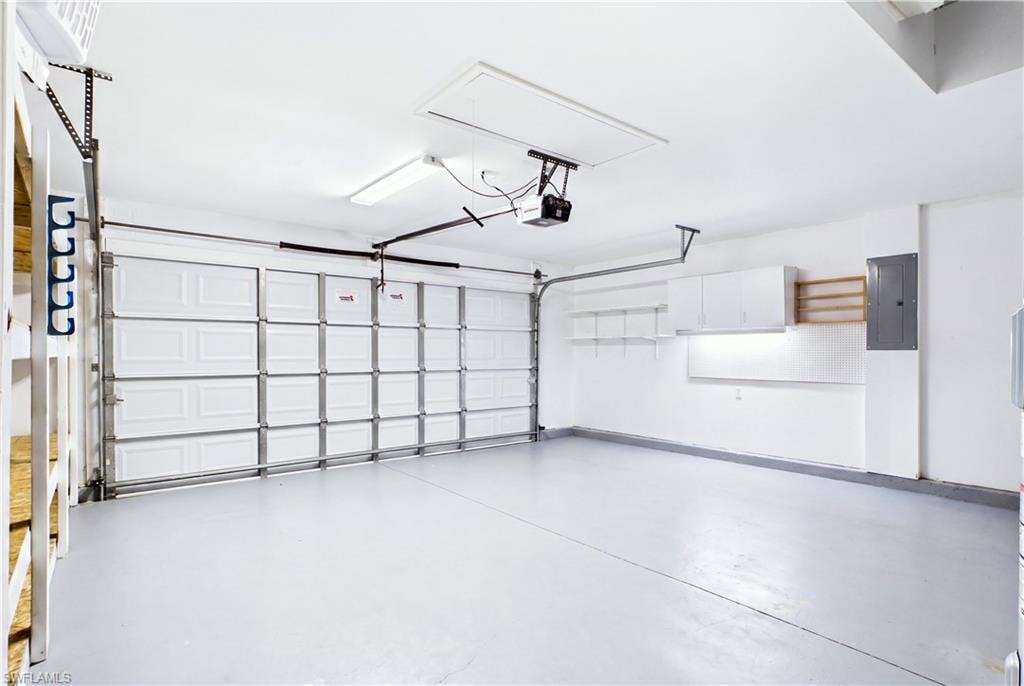 Overhead garage door with automated opener, finished floor, wall-mounted cabinetry, and built-in shelving.