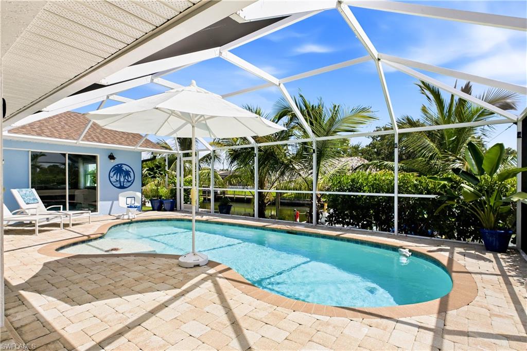 Screened outdoor pool area featuring a freeform pool, paver patio, and mature tropical landscaping.