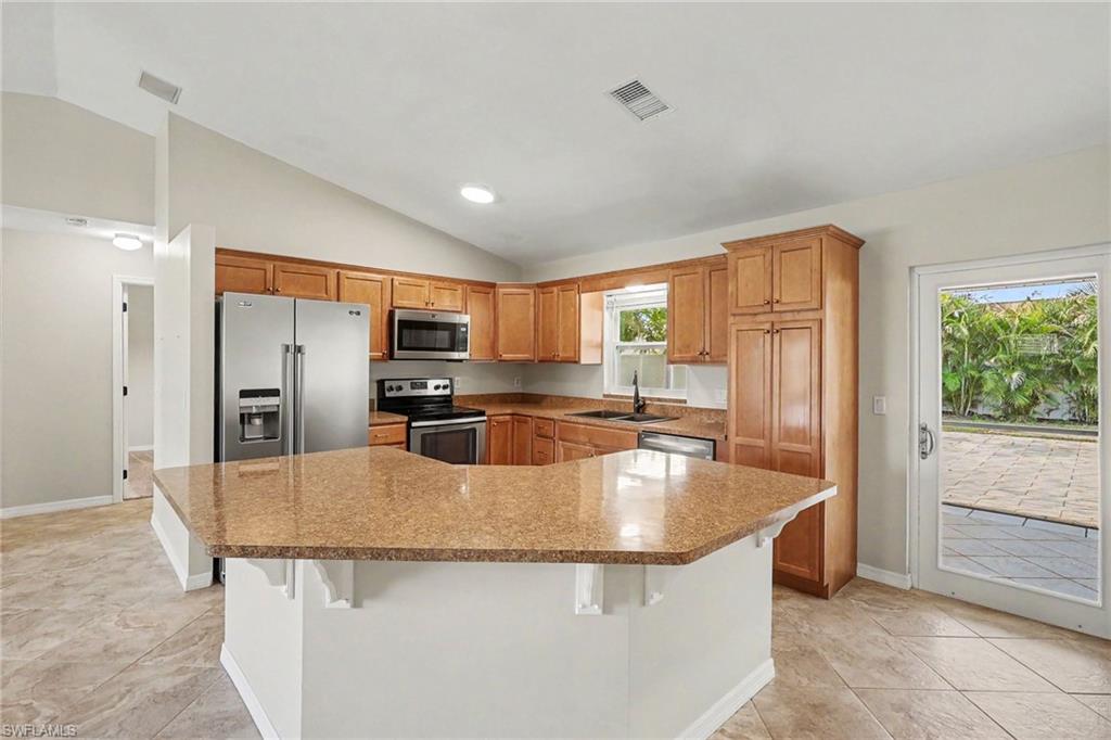 Kitchen featuring wood cabinetry, stainless steel appliances, a breakfast bar with a speckled countertop, and tiled flooring