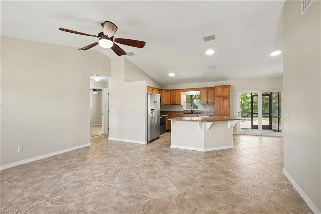 Vaulted ceilings, tile flooring, and a kitchen featuring wood cabinetry, stainless steel appliances, and a breakfast bar