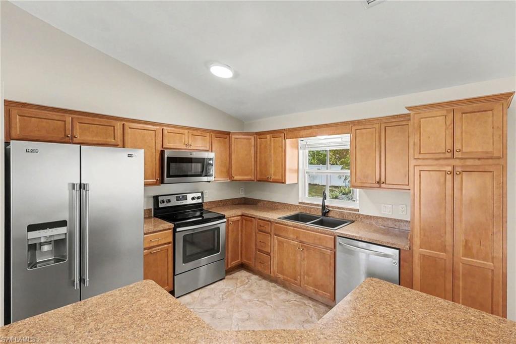Kitchen featuring stainless steel appliances, wood cabinetry, stone-finish countertops, and a double basin sink