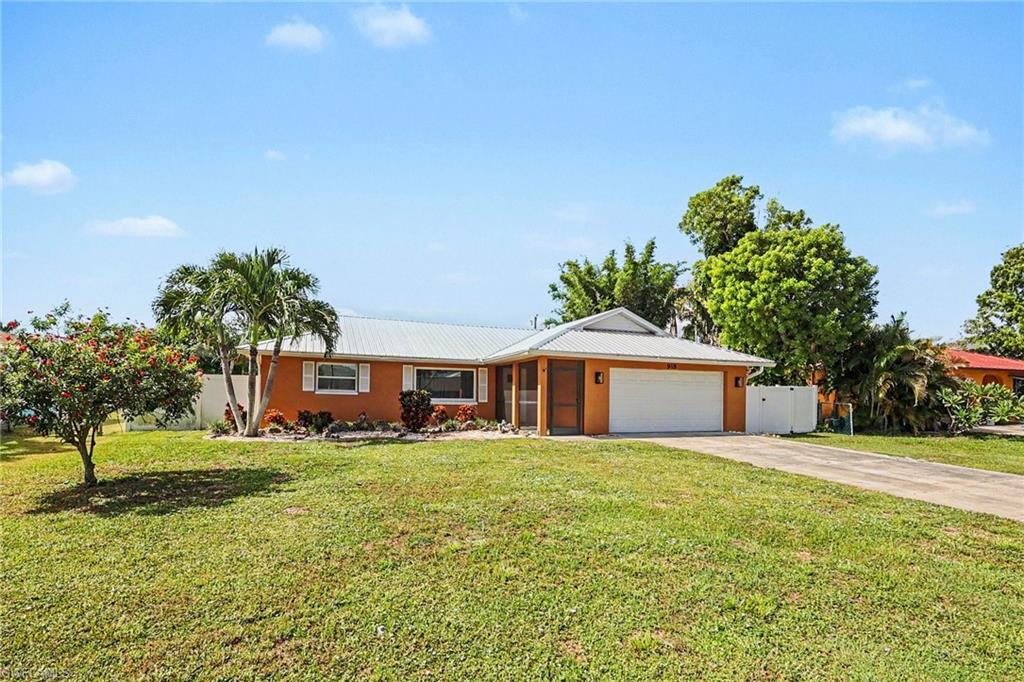 Single-story residence featuring an attached garage, paved driveway, mature palm trees, and front landscaping