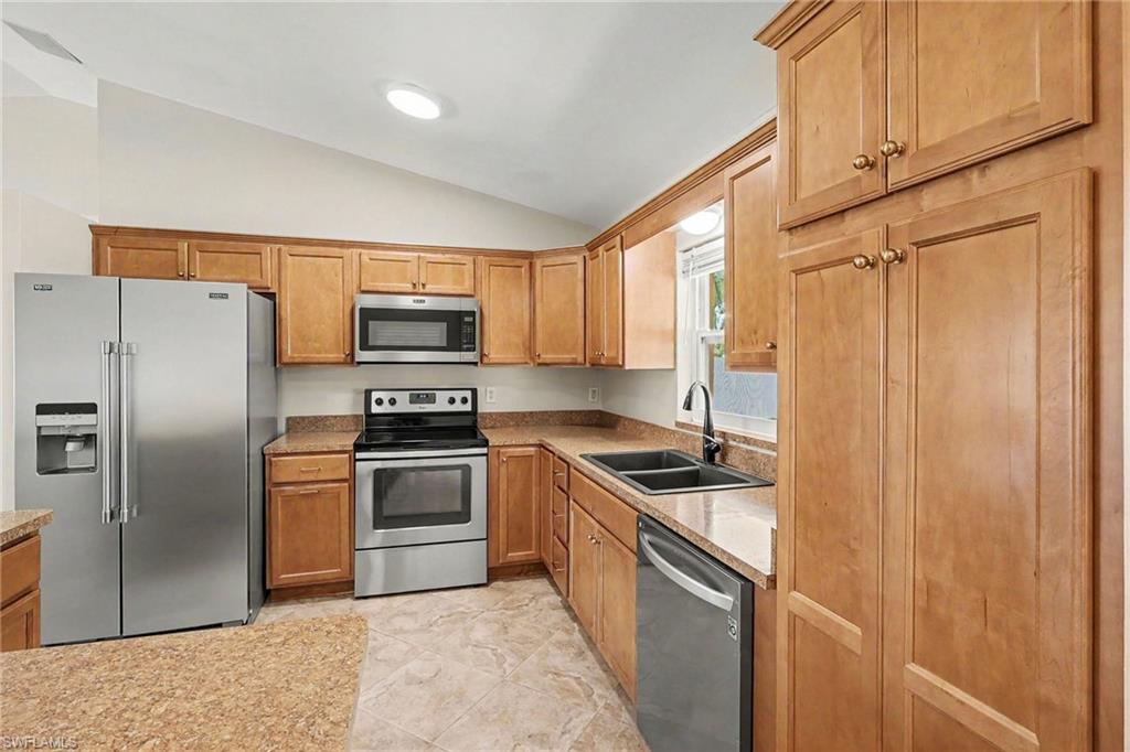 Kitchen featuring wood-finish cabinetry, stainless steel appliances, dual basin sink, and vaulted ceiling