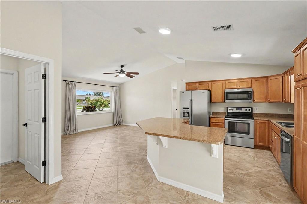 Kitchen featuring wood cabinetry, stainless steel appliances, and a breakfast bar with stone-finish countertops