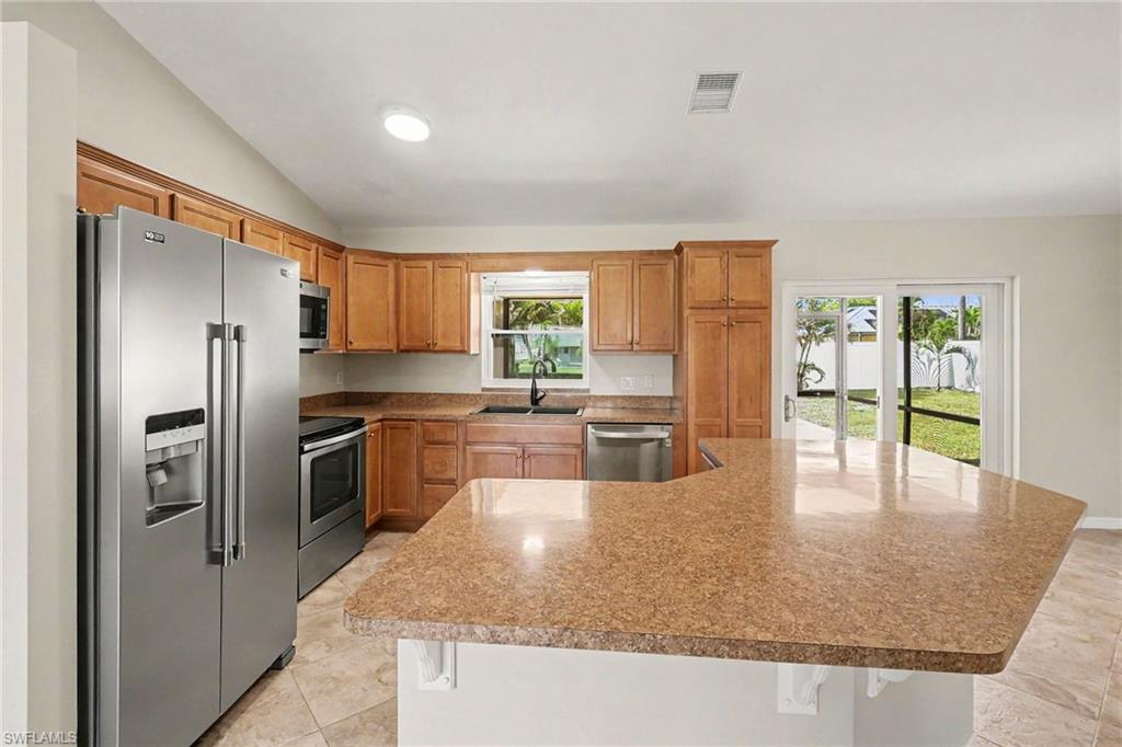 Kitchen featuring stainless steel appliances, wood-finish cabinetry, a large kitchen island, tile flooring, and sliding glass doors