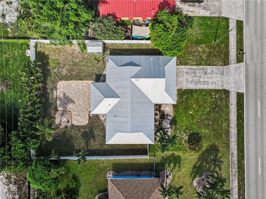 Property with a light-colored hip roof, a concrete driveway, and mature trees
