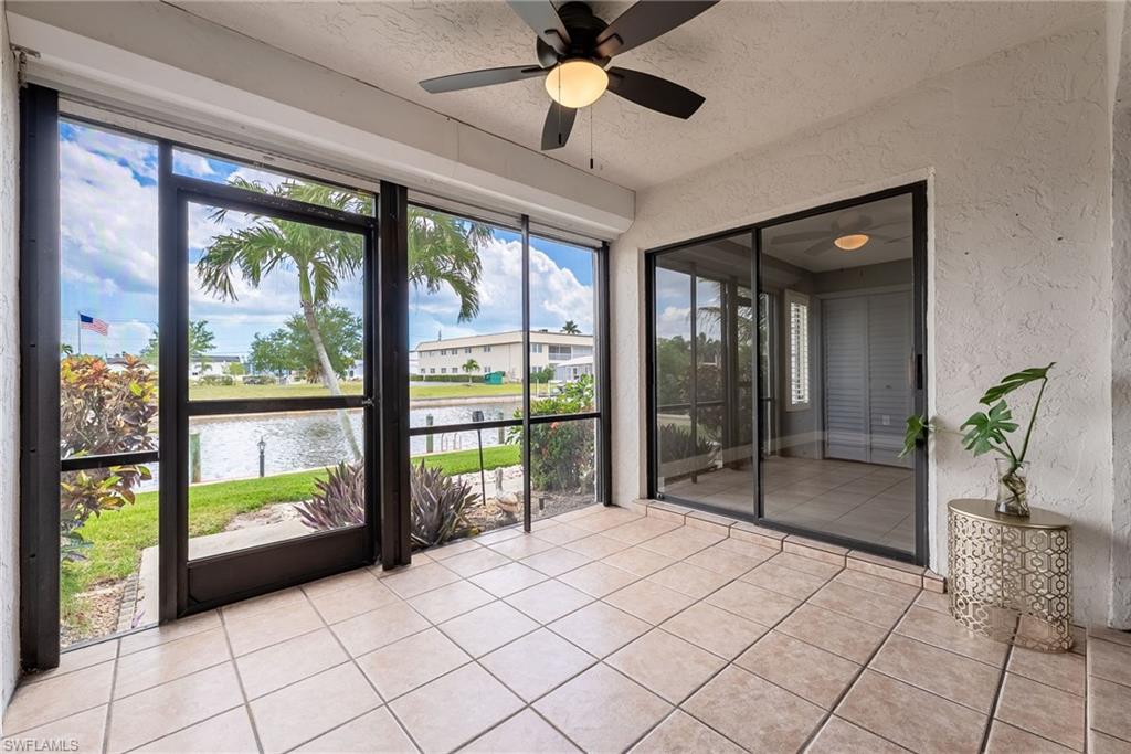 Expansive lanai with diagonal tile flooring, black-framed sliding glass doors, and black-framed screened entry door opening to manicured grounds and waterfront landscape