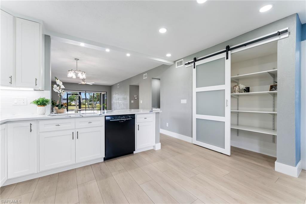 White shaker cabinetry, light wood-finish flooring, recessed lighting, modern barn door, and a built-in shelving unit