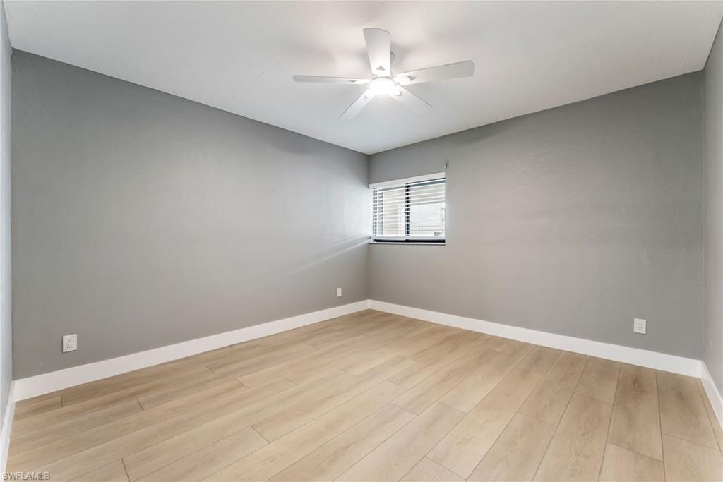 Light wood-finish flooring, neutral gray walls, and a ceiling fan with integrated lighting