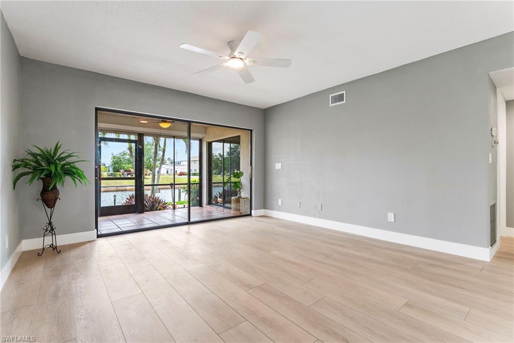 Spacious room featuring light wood-finish flooring, a ceiling fan with integrated lighting, and a vaulted ceiling