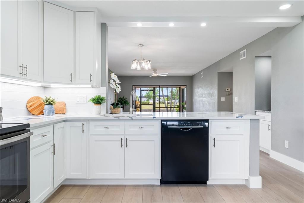 White shaker cabinetry, light-toned wood-finish flooring, white subway tile backsplash, recessed lighting, and a kitchen island with a built-in dishwasher