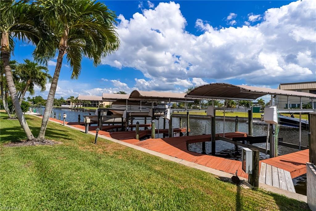 Waterfront property featuring multiple covered boat lifts, a wooden dock, and palm trees