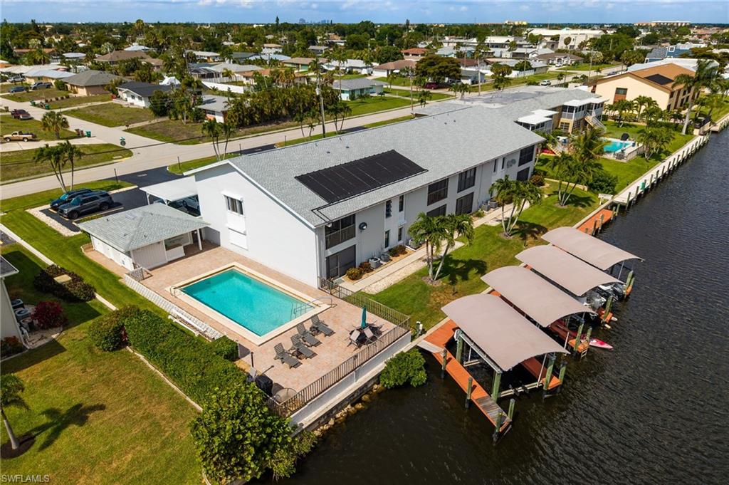 Building exterior with solar panels, a rectangular swimming pool, fenced pool deck, and multiple covered boat slips on a waterway