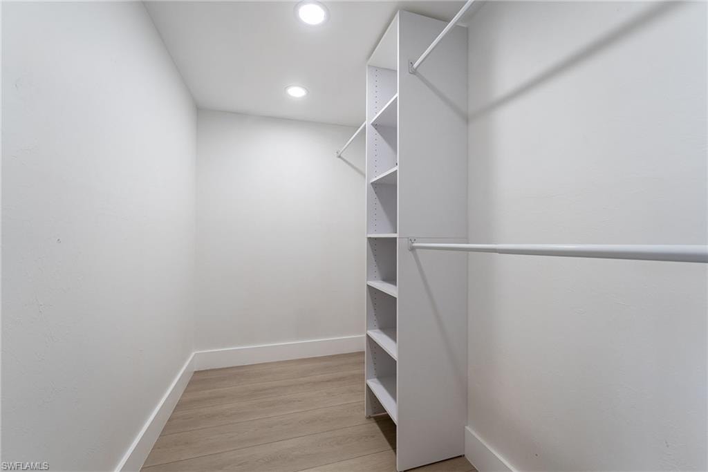 Recessed lighting, wood-finish flooring, white walls, built-in shelving, and two clothing rods