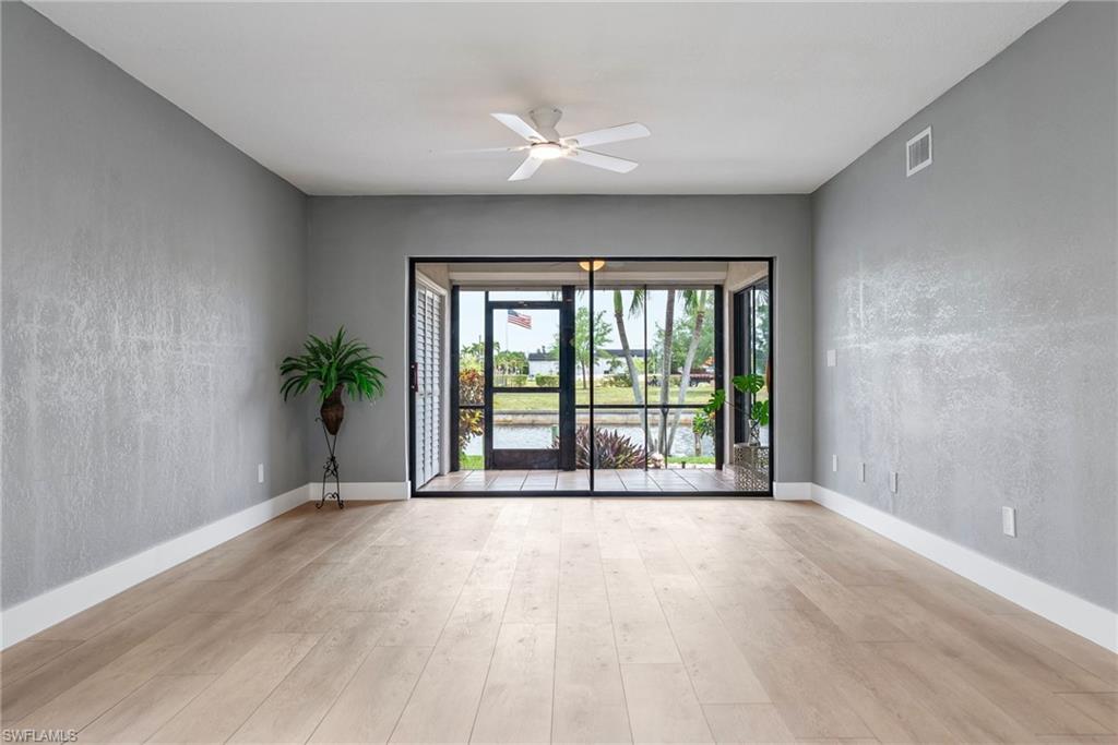 Wood-finish flooring throughout, ceiling fan with integrated lighting, and sliding glass doors opening to an outdoor area with water frontage