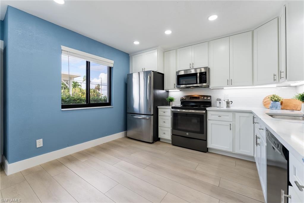 Kitchen featuring light wood-finish flooring, white cabinetry, stainless steel appliances, and a solid surface countertop