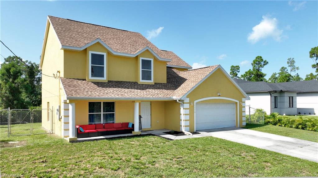 Yellow stucco exterior with white trim, front porch with columns, attached garage, shingle roof, and a fenced side yard