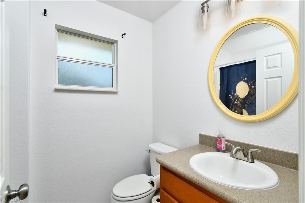 White painted walls, compact window with privacy glass, vanity with an integrated sink, wood-finish cabinetry, and a round mirror