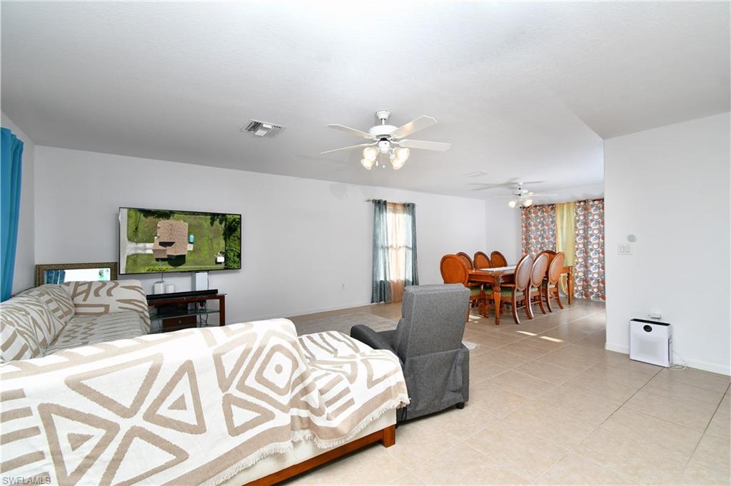 Open-concept living and dining areas featuring tile flooring, multiple ceiling fans, and large windows with privacy drapes