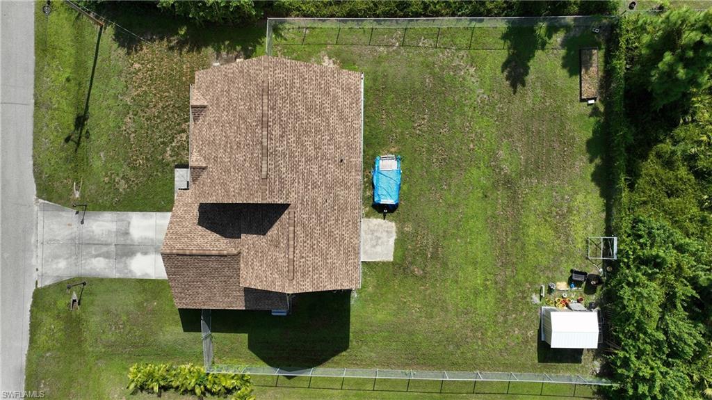 Gabled roofline, concrete driveway, expansive lawn, perimeter fencing, and a detached storage shed
