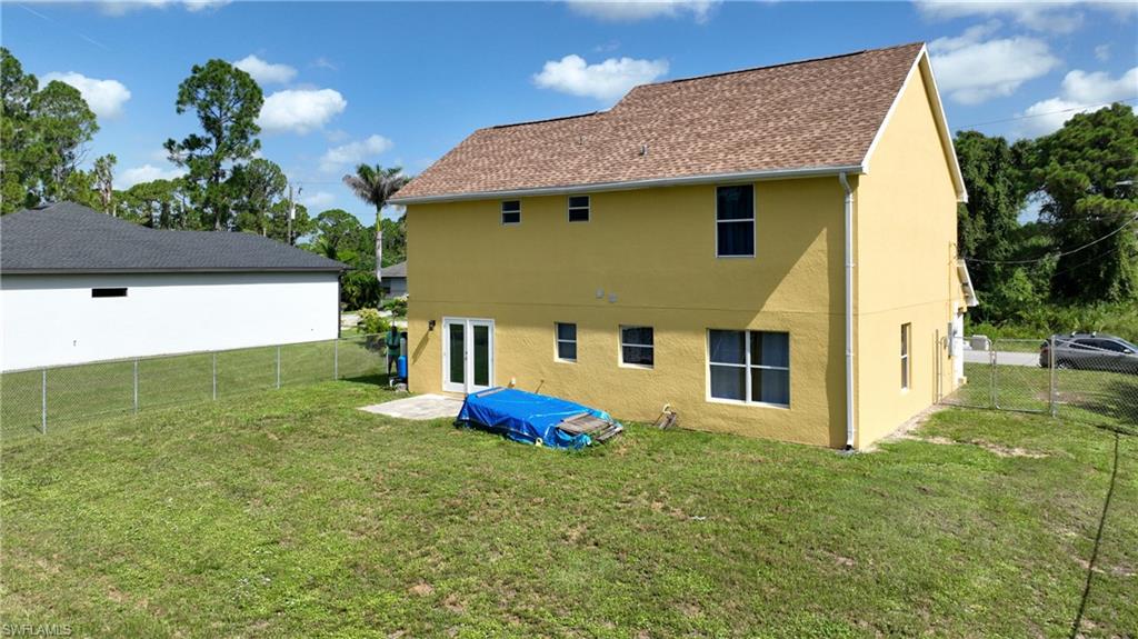 Expansive grassy yard area with a chain-link fence, ground-level patio, and a two-story exterior featuring a shingle roof and multiple windows