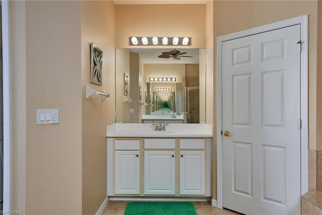 Vanity with a single basin sink, white cabinetry, wall-mounted light bar, and a large mirror