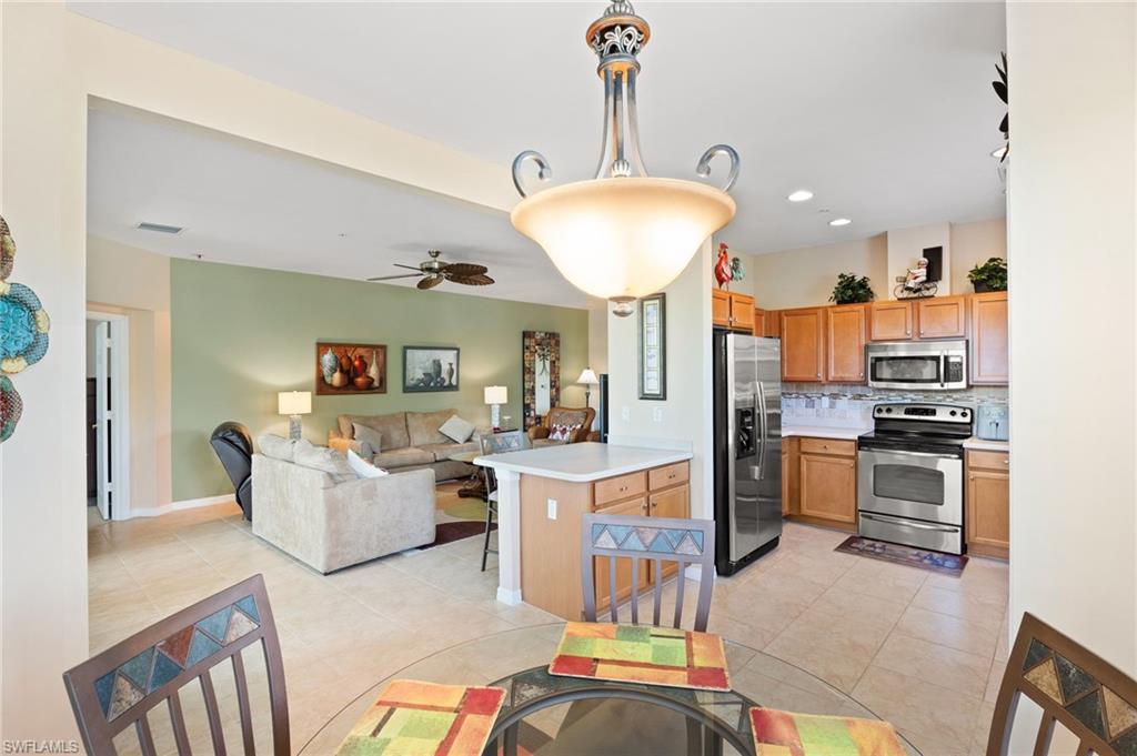 Open-concept kitchen and living area featuring stainless steel appliances, wood cabinetry, a breakfast bar, and tile flooring