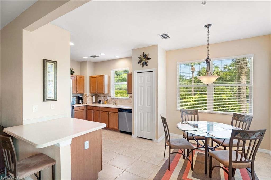 Kitchen featuring wood cabinetry, stainless steel dishwasher, tile flooring, and a breakfast bar with a light-toned countertop