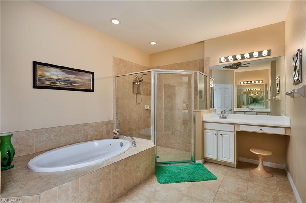 Tiled flooring, built-in soaking tub, glass-enclosed shower, single vanity with integrated sink, and vanity lighting