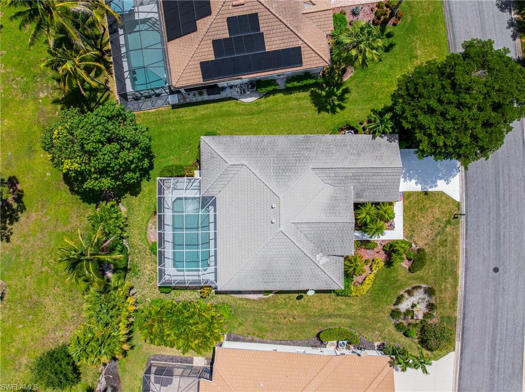 Screened-in pool, mature landscaping, paved driveway, gabled roofline, and front yard with decorative plantings